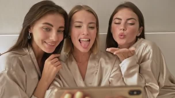 Χαρούμενα αστεία νεαρά κορίτσια φίλες γκρινιάζουν ενώ βγάζουν μια σέλφι στο κινητό στο φωτεινό υπνοδωμάτιο - Πλάνα, βίντεο