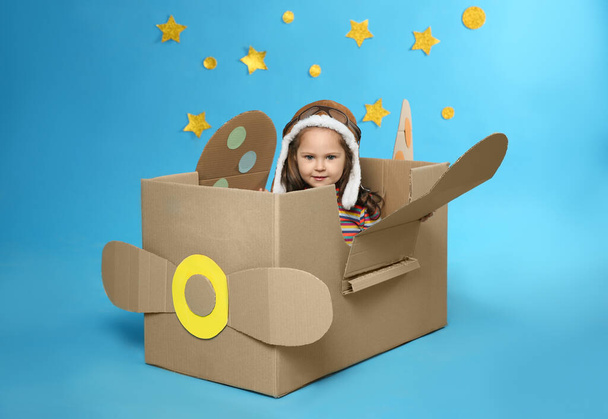 Little child playing with plane made of cardboard box near stars on blue background - Foto, imagen