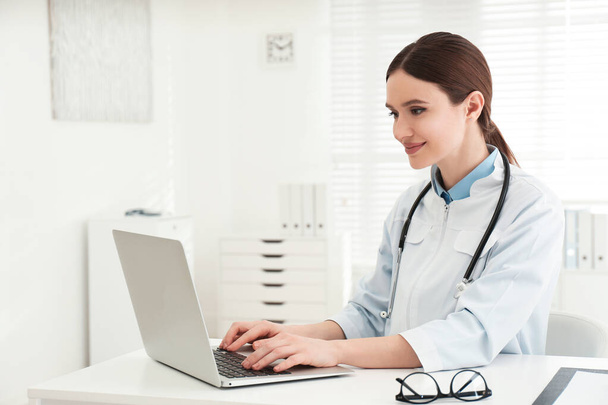 Young female doctor working with laptop at table in office - Photo, Image