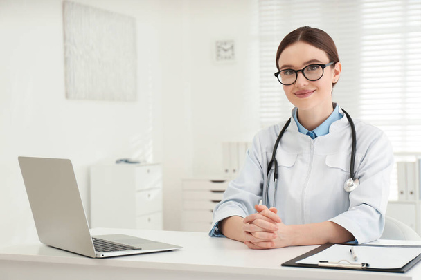 Portrait of young female doctor in white coat at workplace - Photo, Image