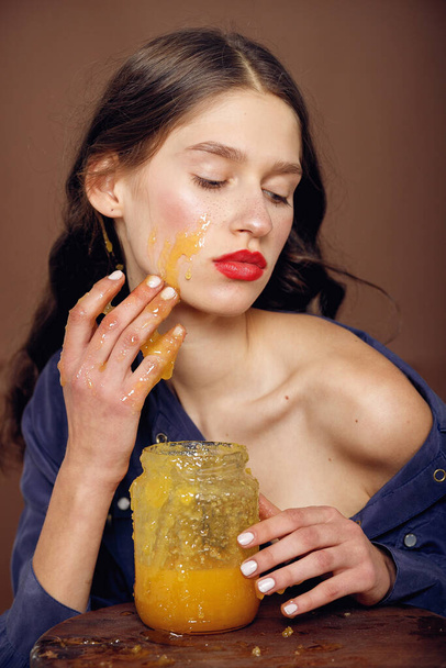 Girl with jar of honey. Healthy food concept, diet, dessert. Beautiful woman with honey on her face. Healthy perfect skin. Honey treatment. - Foto, imagen