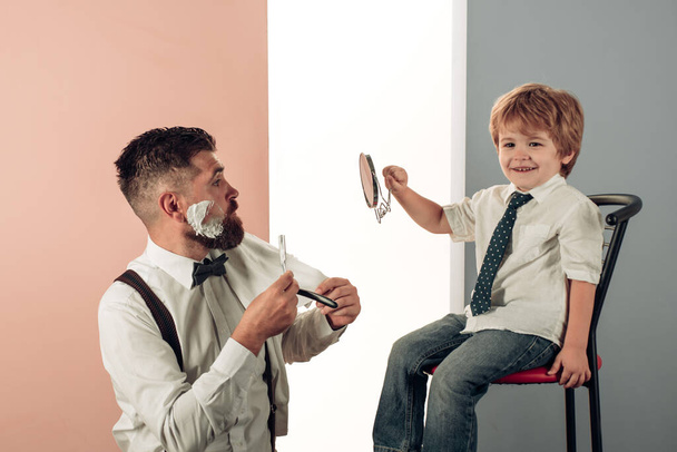 Ο πατέρας μαθαίνει στον γιο να ξυρίζεται. Οικογενειακός χρόνος. Ο γενειοφόρος επισκέπτεται κομμώτρια στο κουρείο. Κρέμα ξυρίσματος. - Φωτογραφία, εικόνα