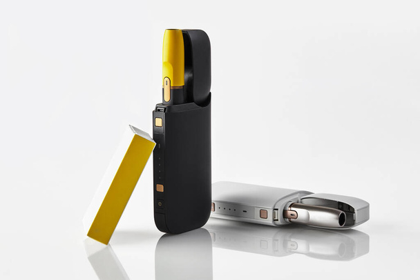 Yeni nesil, açık bataryalarda iki siyah ve sarı elektronik sigara ve beyaz üzerine izole edilmiş kibrit kutusu. Isıtma tütün sistemi. Kapat. - Fotoğraf, Görsel