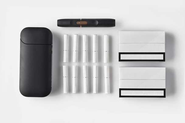 Cigarrillo electrónico negro de nueva generación y batería, dos paquetes y diez heatsticks aislados en blanco. Calefacción sistema de tabaco. De cerca, acostado plano
 - Foto, Imagen