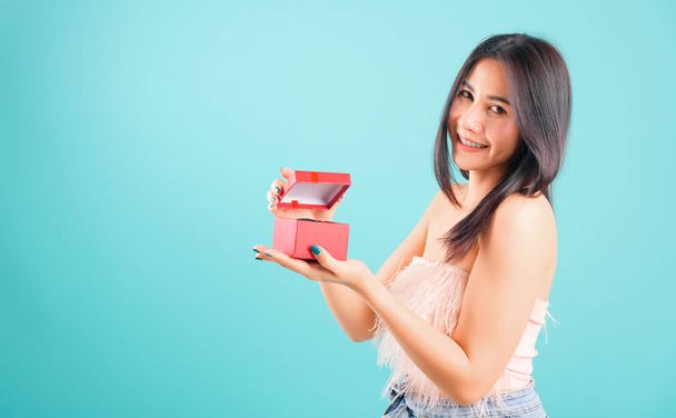 Portrait asian beautiful woman with hat her opening red gift box and her looking to gift box also on blue background, with copy space for text - Foto, afbeelding
