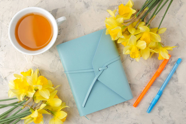 Flores de primavera, narcisos amarelos e uma xícara de chá, um caderno sobre um fundo de concreto leve. vista superior
 - Foto, Imagem