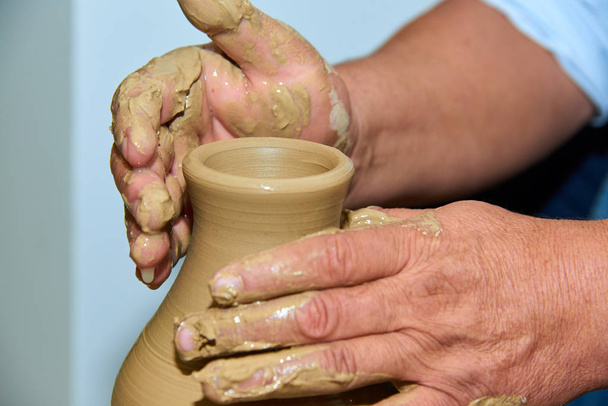 Ręce garncarza. Garncarz robi ceramiczny wazon na kole garncarskim. Tworzenie wazonu z gliny zbliżenie.   - Zdjęcie, obraz