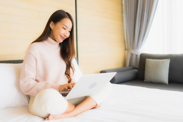 Porträt schöne junge asiatische Frau mit Laptop und Handy auf dem Bett im Schlafzimmer - Foto, Bild