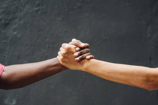 Δύο χέρια μαζί από έναν Αφρικανό και έναν Καυκάσιο. - Φωτογραφία, εικόνα