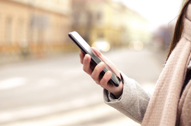 Zavřít obrázek černého mobilního telefonu v ženské ruce na ulici ve městě s rozmazaným pozadím - Fotografie, Obrázek