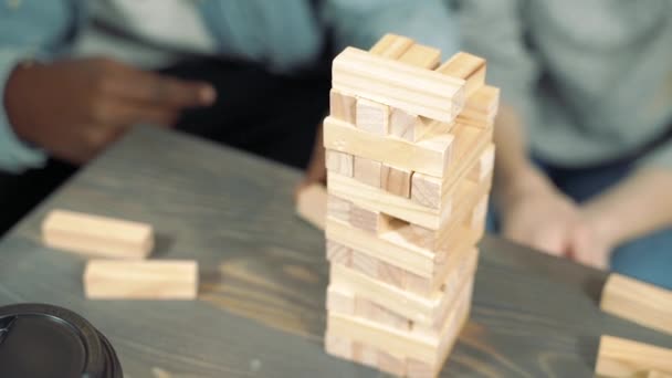 Tower of wooden blocks. Close-up hands of friends playing block removal game on a table. - Video