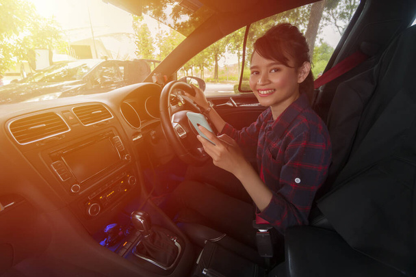 E-χαιρετισμό έννοια, χαριτωμένο κορίτσι της Ασίας μέσα στο αυτοκίνητο χαμογελώντας και κοιτάζοντας την κάμερα κρατώντας smartphone - Φωτογραφία, εικόνα