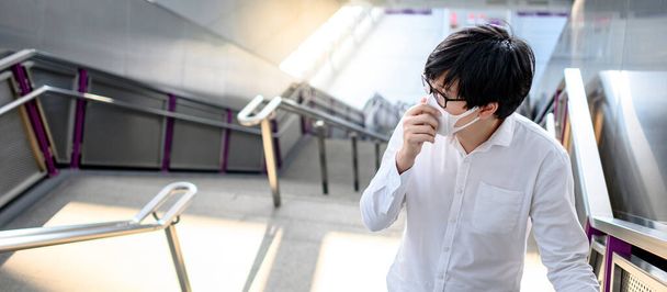 スカイトレイン駅や都市鉄道のホームでフェイスマスクを身に着けているアジア人男性。武漢コロナウイルス(COVID-19)公共交通機関での感染予防。PM2.5大気汚染防止のための健康意識. - 写真・画像