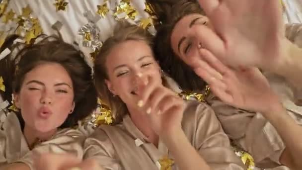 Top kilátás boldog mosolygós fiatal lányok barátok fekszenek az ágyon konfettivel a világos hálószobában - Felvétel, videó