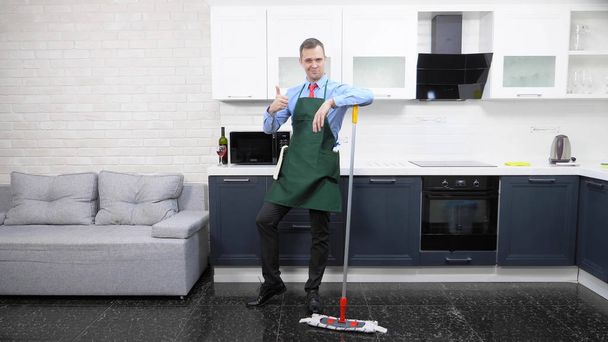  pohledný muž v kravatě a zástěře utírá podlahu v kuchyni - Fotografie, Obrázek