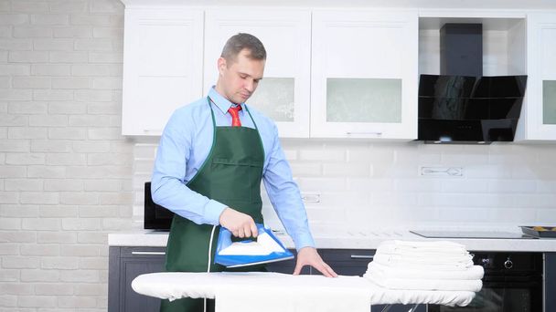 handsome man in a tie and apron ironing linen. cleaning concept - Foto, imagen