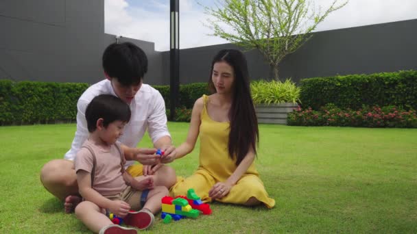Schattig klein Aziatisch kind spelen speelgoed blok in de tuin met familie samen. Papa, zwangere vrouw of mama die speelt met een geliefde schattige zoon. Vader, moeder wordt gelukkig met kind op vakantie weekend. gelukkig gezin - Video