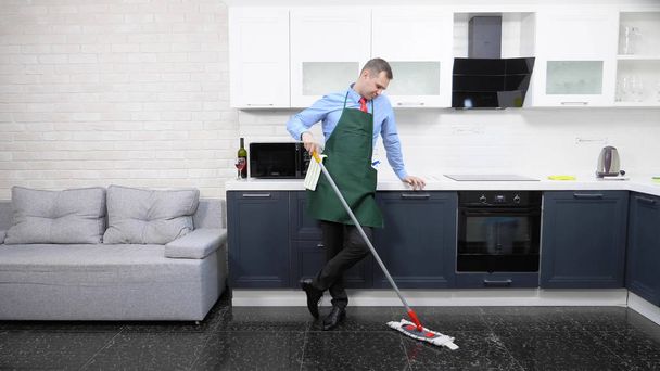  schöner Mann in Krawatte und Schürze wischt den Boden in der Küche - Foto, Bild