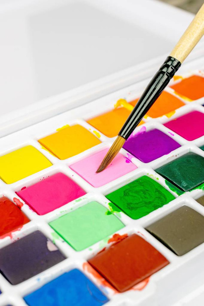 Ein Künstler bemalt Pinsel und eine Schachtel mit bunten Aquarellfarben - Foto, Bild