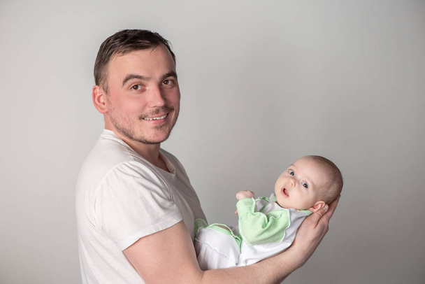 Handsome man father holding a cute little smiling baby in his arms on a gray background - Zdjęcie, obraz