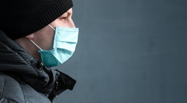 homem em azul máscara médica protetora na cidade em um fundo cinza
 - Foto, Imagem