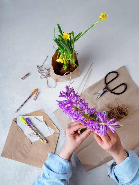 Woman in casual clothes packing spring potted flowers in brown paper as gifts, top view, vertical orientationorientation - Photo, Image