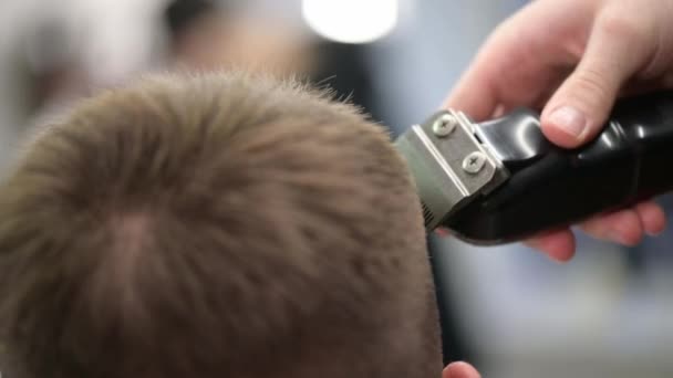 Młody fryzjer w Barbershop. Zbliżenie mistrza strzyżenia włosów z przycinaczem - Materiał filmowy, wideo