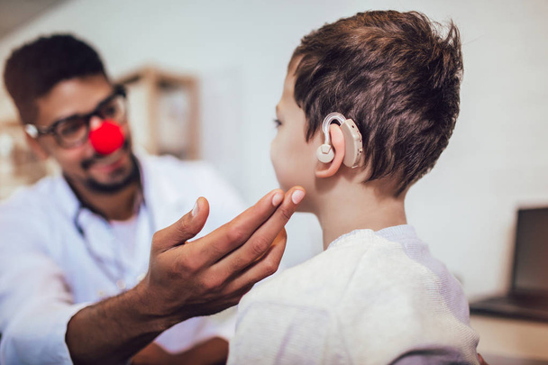 Glimlachende dove jongen met oorimplantaat bij de dokter. - Foto, afbeelding
