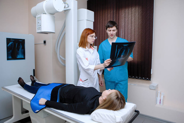 Γυναίκες και άνδρες ακτινολόγοι εξετάζουν ακτινογραφίες κοντά σε ασθενή σε ιατρικό γραφείο. - Φωτογραφία, εικόνα