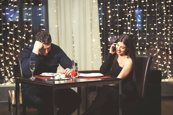 レストランのテーブルで夫婦が葛藤する。スマートフォンで話している女性、男はミス. - 写真・画像
