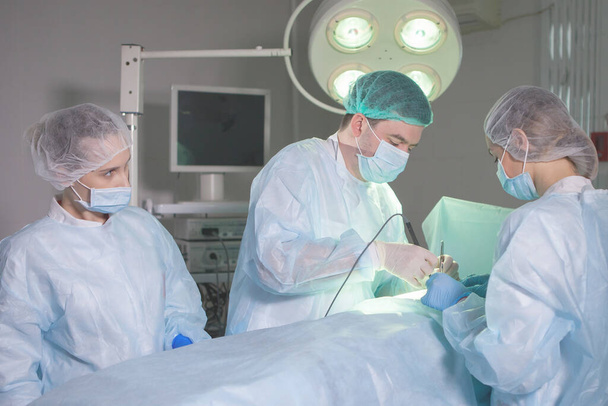 Tre chirurghi durante la chirurgia addominale. Uniformi blu, guanti di lattice, strumenti medici. Illuminazione spot. - Foto, immagini