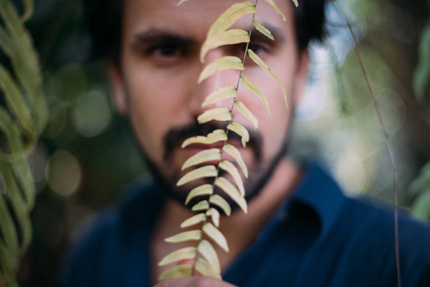 Conceptual portrait of a man in green leaves. Beautiful brunette guy, model posing among tropical thickets. Close-up - Photo, Image
