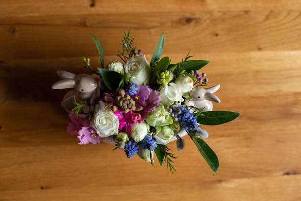 σε ένα ξύλινο τραπέζι είναι ένα λουλουδάτο μπουκέτο που συμπληρώνεται από ειδώλια του Πάσχα λαγούς - Φωτογραφία, εικόνα