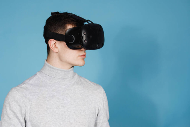 Joven juega con gafas de realidad virtual. Juegos de ordenador, fondo azul, emociones. - Foto, Imagen