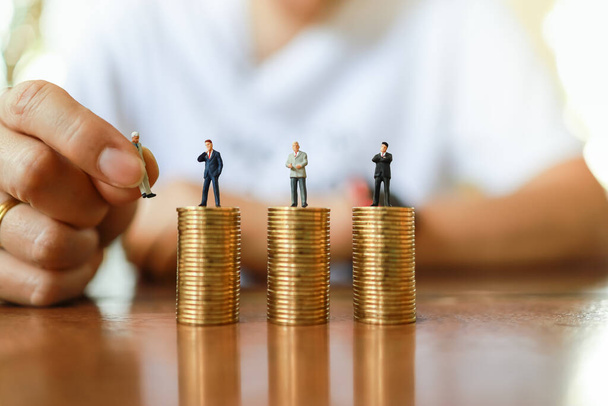 Business, Money and Human Management Resource Concept. Close up of man hand holding businessman miniature figure people and putting to change figure on top od stack of gold coin on wooden table. - Photo, Image