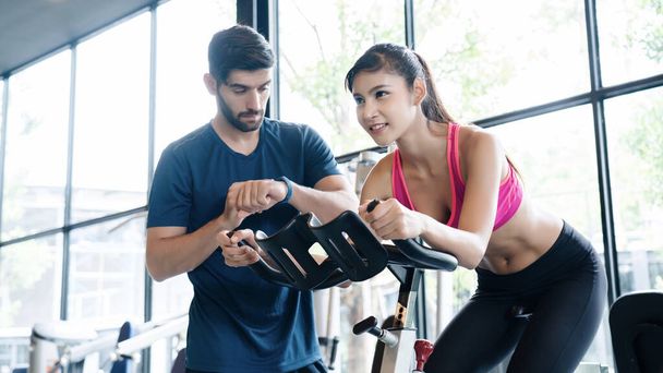 Asian Women wear sportswear, workout ride bicycles in gym, with the intention of health care. With a trainer to advise By cycling to make the body healthy With tight muscles And reduce the weight good - Foto, Imagen