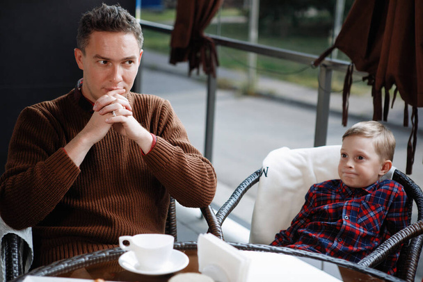 Father and son are sitting at a table in a cafe. Parental love, happy childhood, child care. - 写真・画像