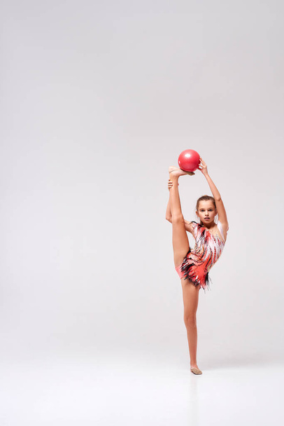 Keep balance. Full-length shot of flexible cute girl child gymnast doing acrobatic exercise using ball isolated on a white background. Sport, training, rhythmic gymnastics concept - Foto, afbeelding