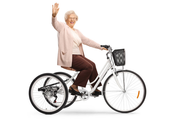 Senior woman riding a tricycle and waving at the camera isolated on white background - Foto, Imagem