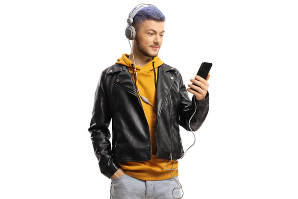 Young guy holding a mobile phone and listening to music on headphones isolated on white background - Фото, изображение