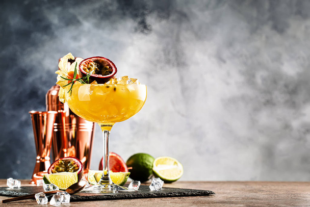 Alcoholic cocktail with fresh passion fruit with rosemary and ice. Gray wood background, bar tools, copy space - Foto, immagini