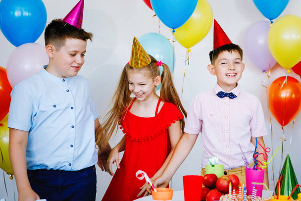 Дети на праздновании дня рождения с мячами, кепками, сладостями и смехом. - Фото, изображение