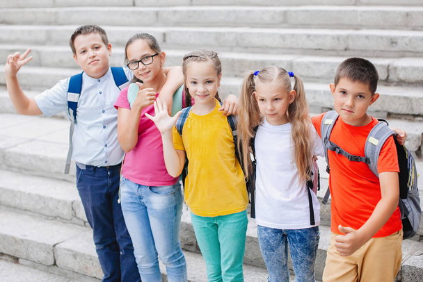 Дети-подростки в разноцветной одежде с рюкзаками поднимаются по лестнице в школу
. - Фото, изображение