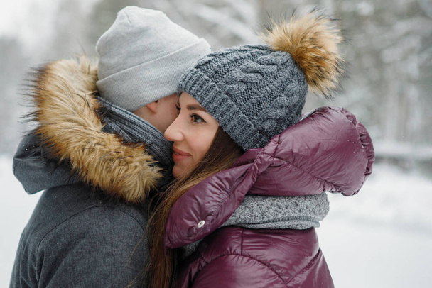 Kochająca para całuje się w zimowym parku na świeżym powietrzu. Ciepłe ubrania, dzianiny kapelusze, zaspy śnieżne, drzewa, zamazane tło. - Zdjęcie, obraz