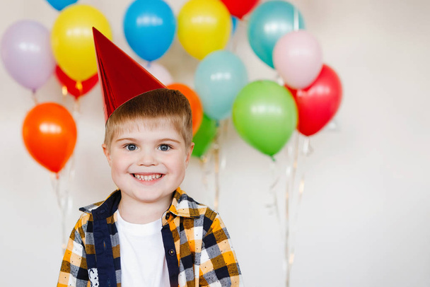 Junge mit Mütze bläst Geburtstagskerze auf Kuchen aus. - Foto, Bild