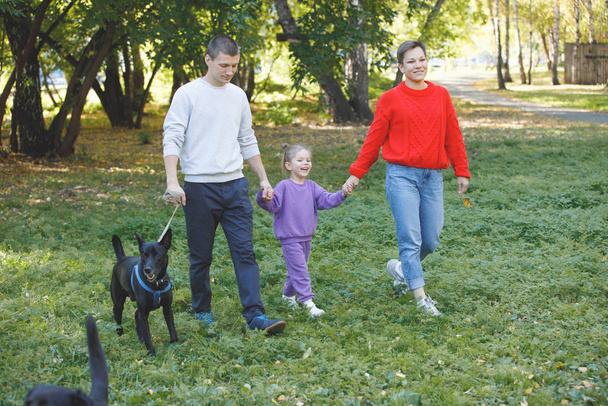 Young family of three: mom, dad and daughter are walking in the park with dogs. - Fotoğraf, Görsel
