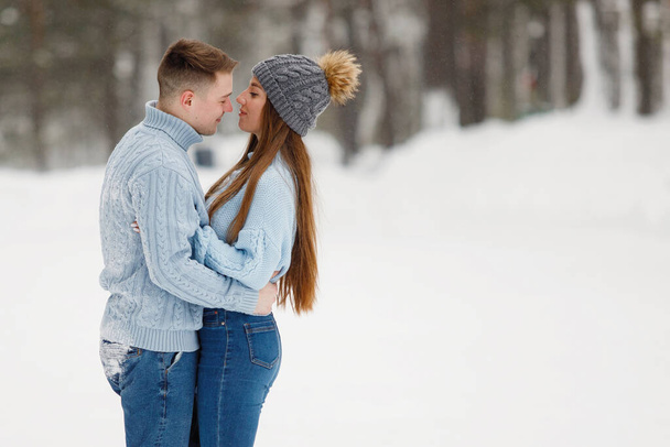 Loving couple hugging in a winter park outdoors. Warm clothes, knitted hats, snowdrifts, trees, blurred background. - Photo, Image