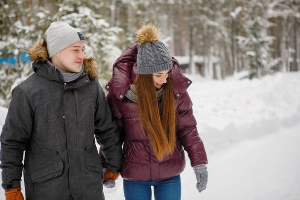 Junges Paar auf der Eisbahn im Winterpark. Warme Kleidung, Strickmützen, Schneewehen, Bäume, verschwommener Hintergrund. - Foto, Bild