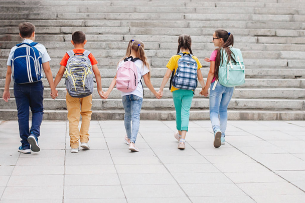 Crianças adolescentes em roupas coloridas com mochilas estão subindo as escadas para a escola. Visão traseira. - Foto, Imagem