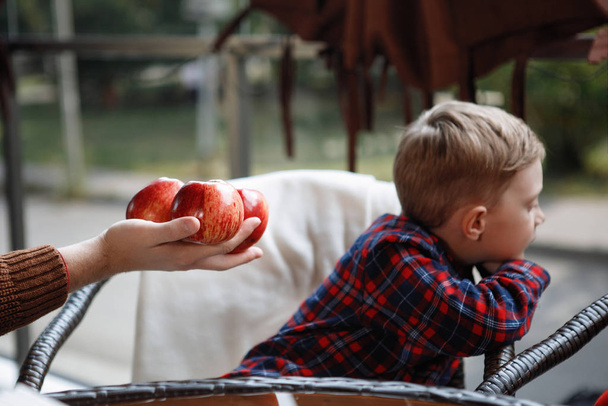Il ragazzo è offerto di mangiare mele rosse a un tavolo in un caffè. Si voltò e fu triste.
. - Foto, immagini